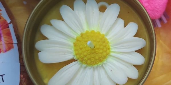 A candle shaped like a white daisy flower with a yellow center.