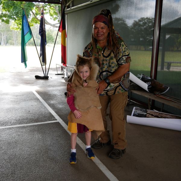 A man and child pose together, child wrapped in a traditional animal skin cloak.