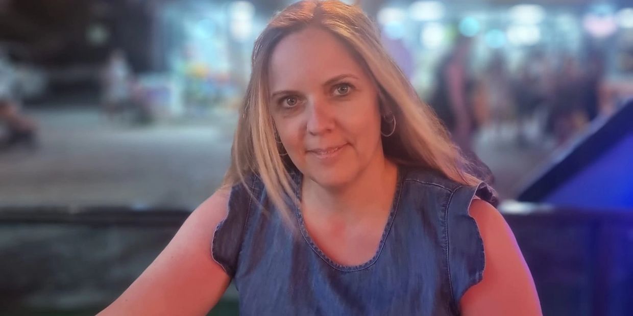 Woman in a denim dress looking at a menu outdoors at night.