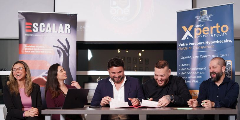 Five professionals smiling and signing documents at a business event.