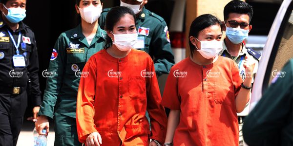 Two women in orange prison uniforms escorted by officers.