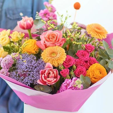 Colorful bouquet with roses, tulips, and other vibrant flowers wrapped in pink paper.