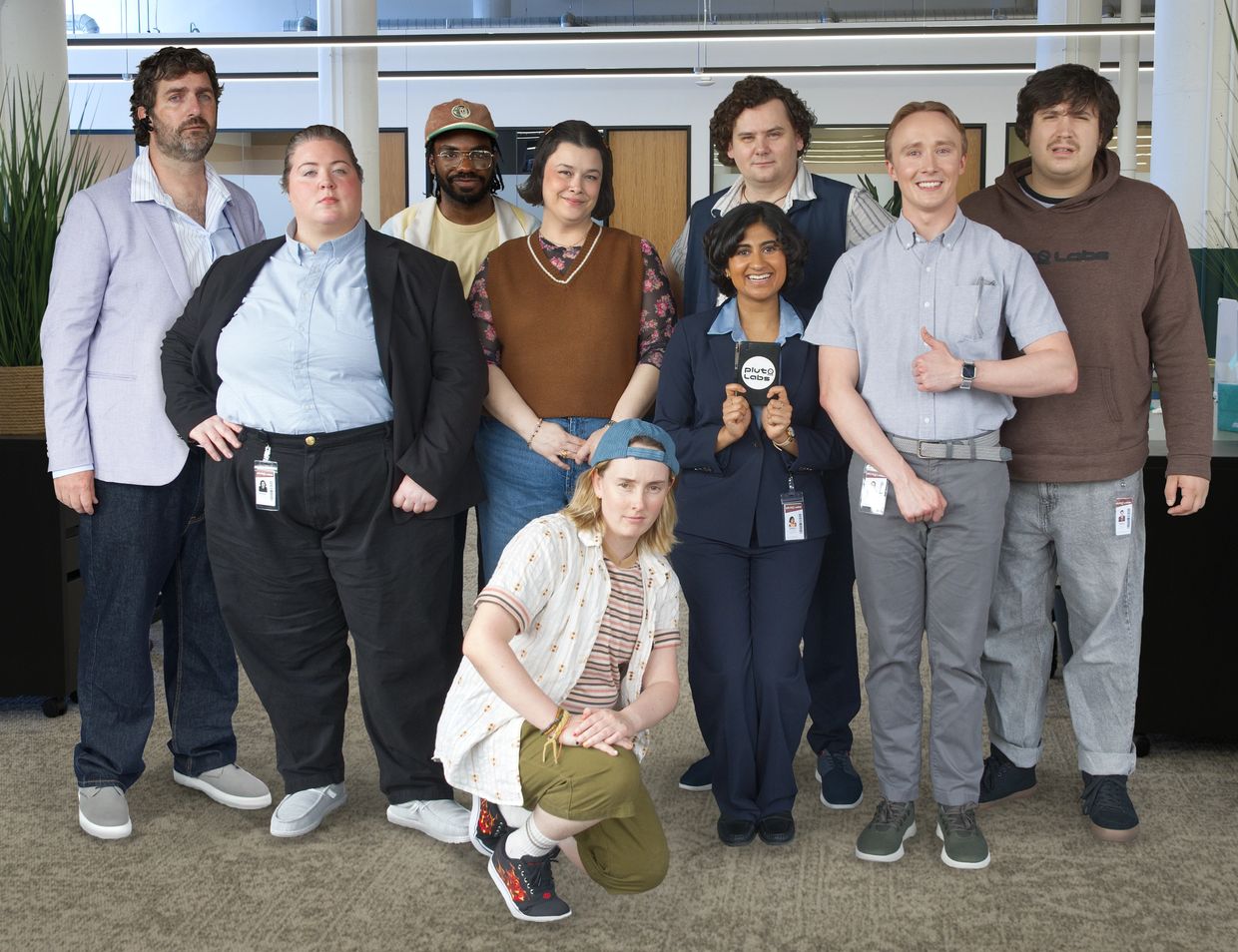 A diverse group of nine coworkers posing together in an office setting.