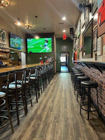Empty sports bar with wooden floors and multiple bar stools.