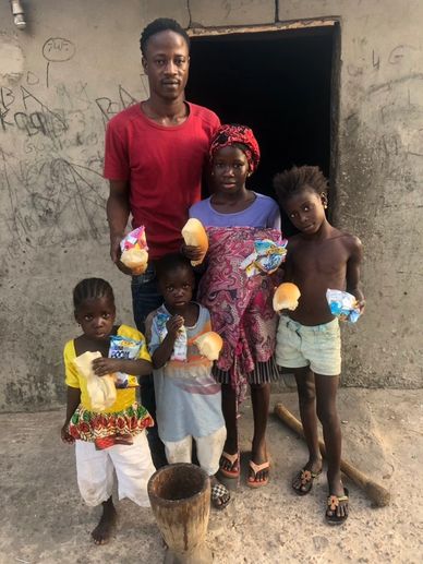 A man and four children holding bread and snacks in front of a concrete building.