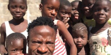 A group of smiling children and a man posing outdoors in sunlight.