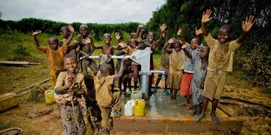 Children joyfully gather around a clean water pump in a rural village.
