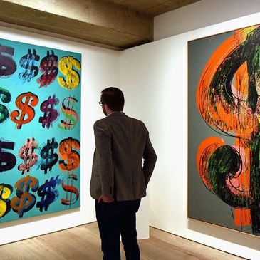 Person observing colorful dollar sign artworks in a gallery.