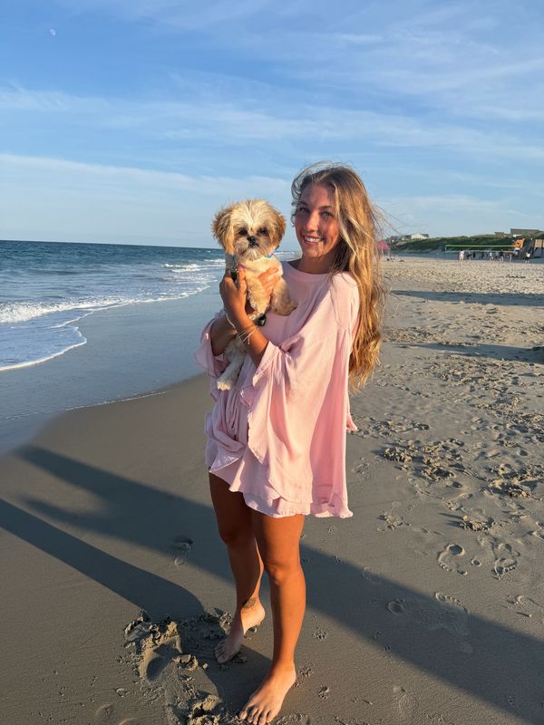 Woman holding dog on the beach with ocean background.
