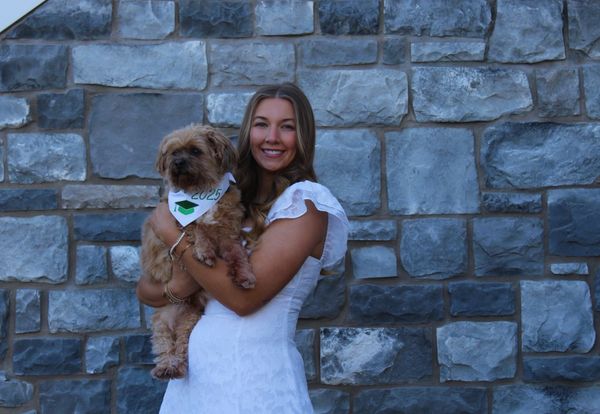 Woman in white dress holding a small dog against a stone wall.