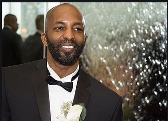 Man in a tuxedo with a boutonniere smiling.