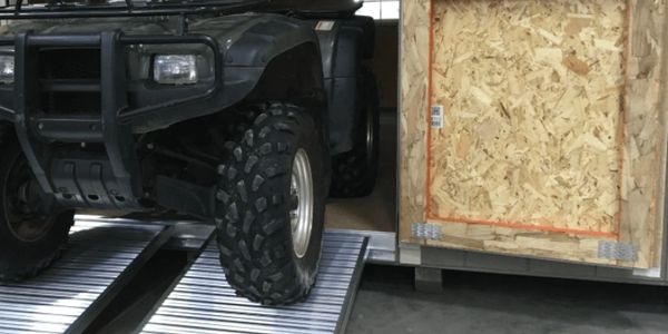 Large off-road vehicle wheel on metal ramps next to a wooden crate.