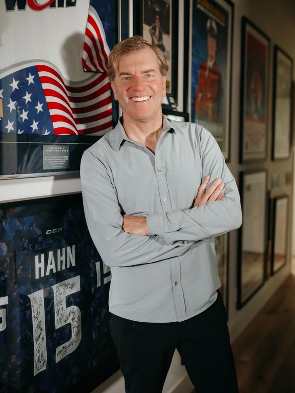Smiling man in a light gray shirt stands with arms crossed near signed sports memorabilia.