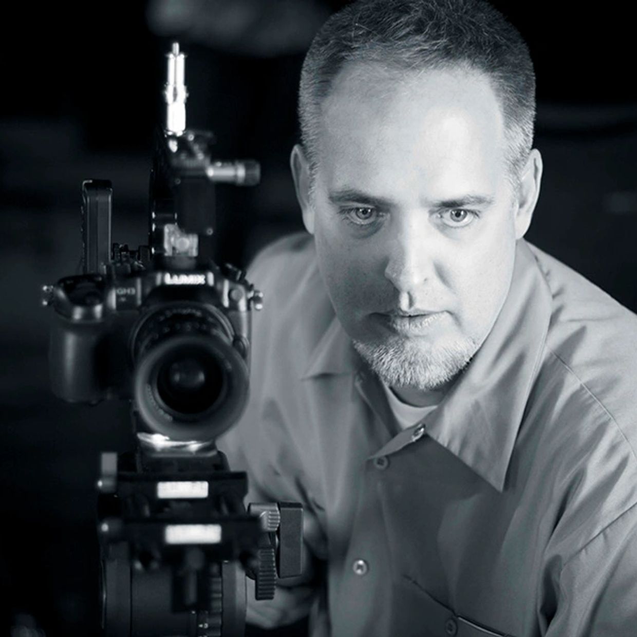 Man focusing intently behind a professional camera setup in black and white.