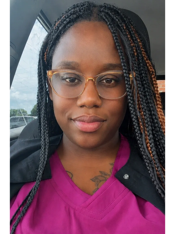 Woman with braided hair and glasses smiling in a car.