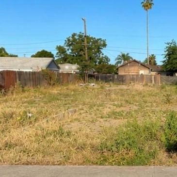 Empty plot of land with dry grass and a few houses in the background.