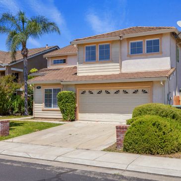 Two-story suburban house with a garage and palm trees on a sunny day.