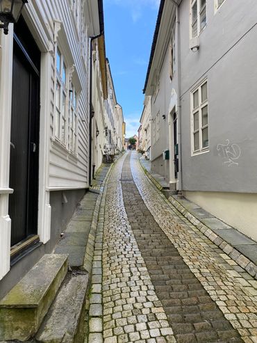 Narrow cobblestone street between white buildings on a clear day.