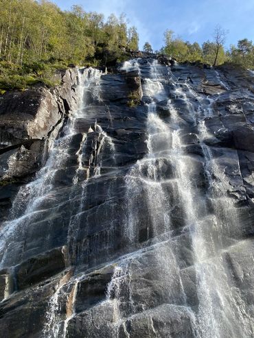 Water cascading down a rocky cliff surrounded by trees under a clear sky.