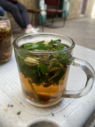 A glass cup of herbal tea with fresh green leaves inside.