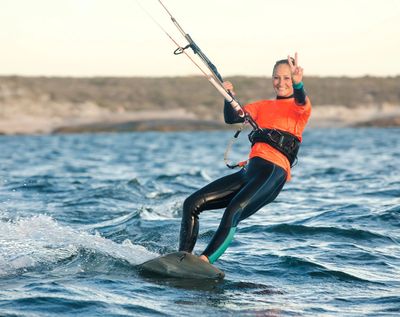 Woman kiteboarding and making a peace sign on the water.