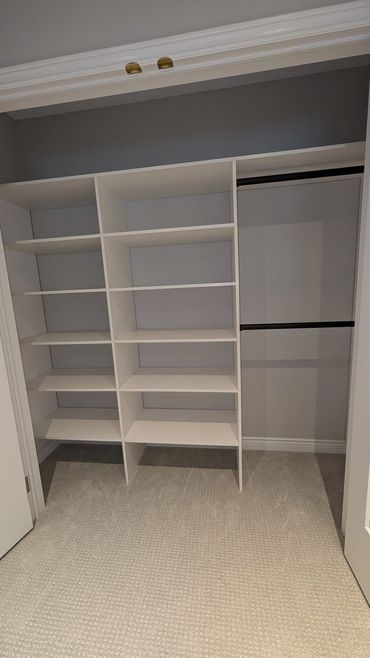 Empty white closet shelves with hanging rods in a carpeted room.closet designs,custom closets, organized spaces.