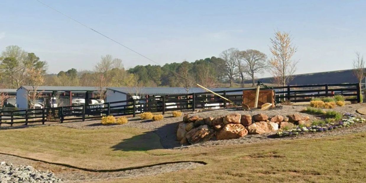 Rustic outdoor area with stone arrangement and fenced structures in the background.