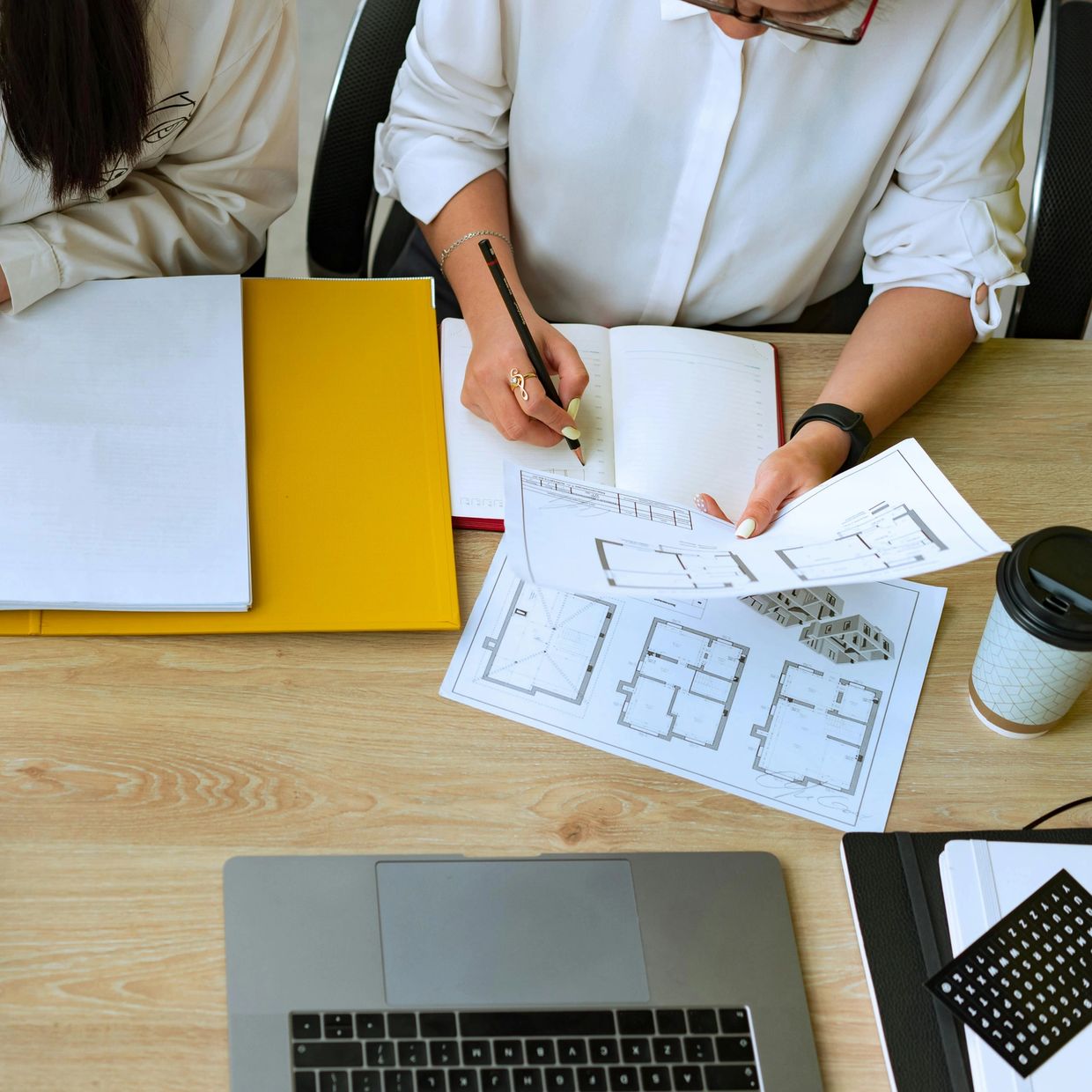 Two people working with documents and architectural plans at a desk.