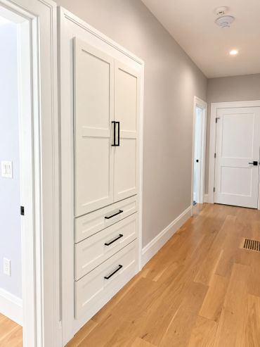 Hallway with built-in storage cabinets and wooden flooring.