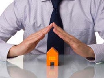 Person protecting a small orange house model with hands.