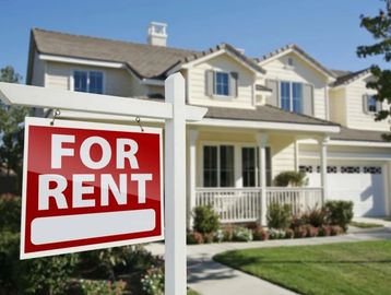 A house with a 'For Rent' sign in front on a sunny day.