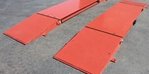 Two long, red metal ramps placed on a concrete surface.