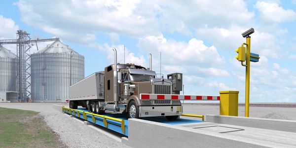 A semi-truck on a weighbridge near silos under a partly cloudy sky.