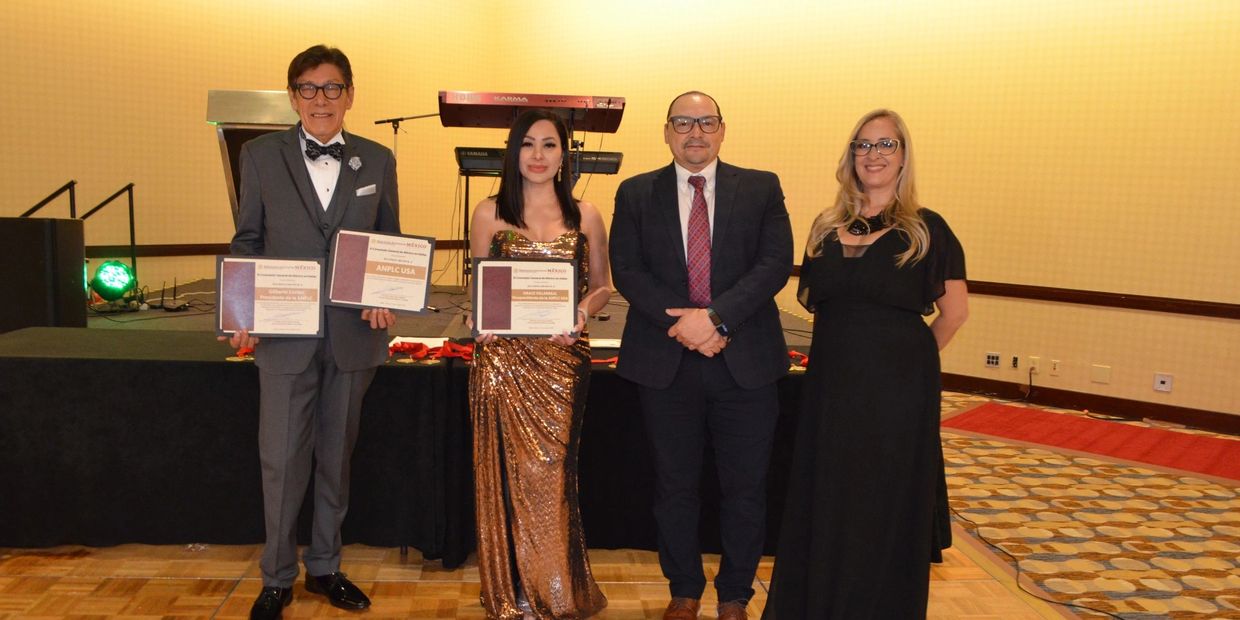 Four formally dressed individuals posing with certificates in an event hall.