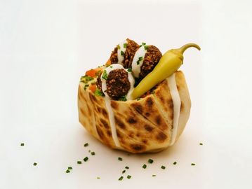 Signature falafel pita: crispy bites, fresh veggies, tahini drizzle & pepper—pure plant-based flavor