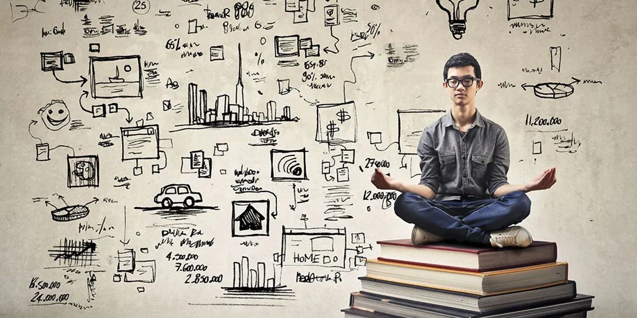 A young man meditates on a stack of books with business sketches on the wall.