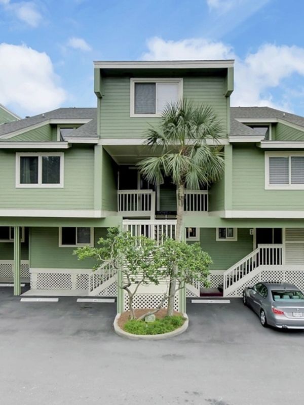 Green house with palm tree and parking spaces.