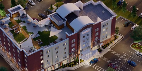 Aerial view of a modern hotel with rooftop seating and parking lot.
