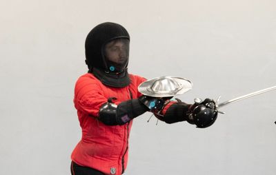Person in protective fencing gear with sword and shield.