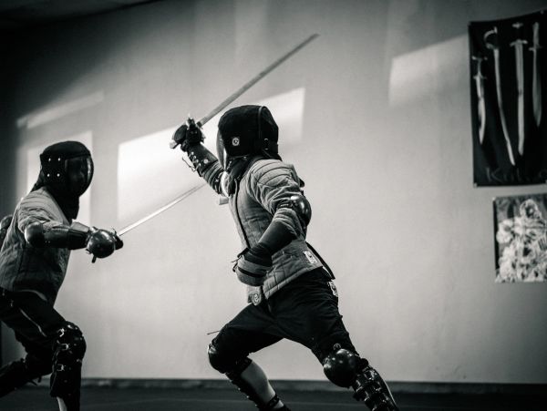 Two people fencing in protective gear indoors.
