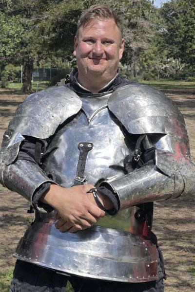 Man smiling in shining metal armor outdoors.