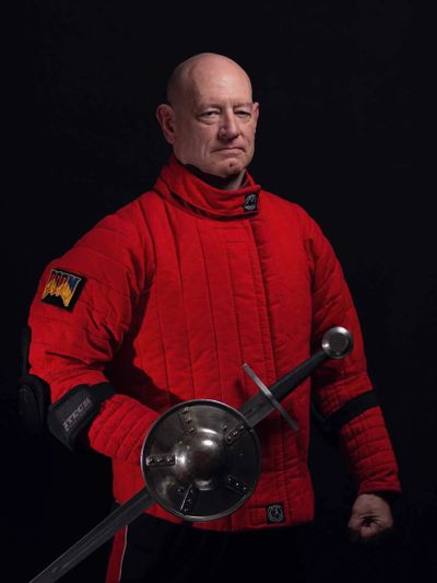 Man in red protective gear holding a sword and shield, posing confidently.