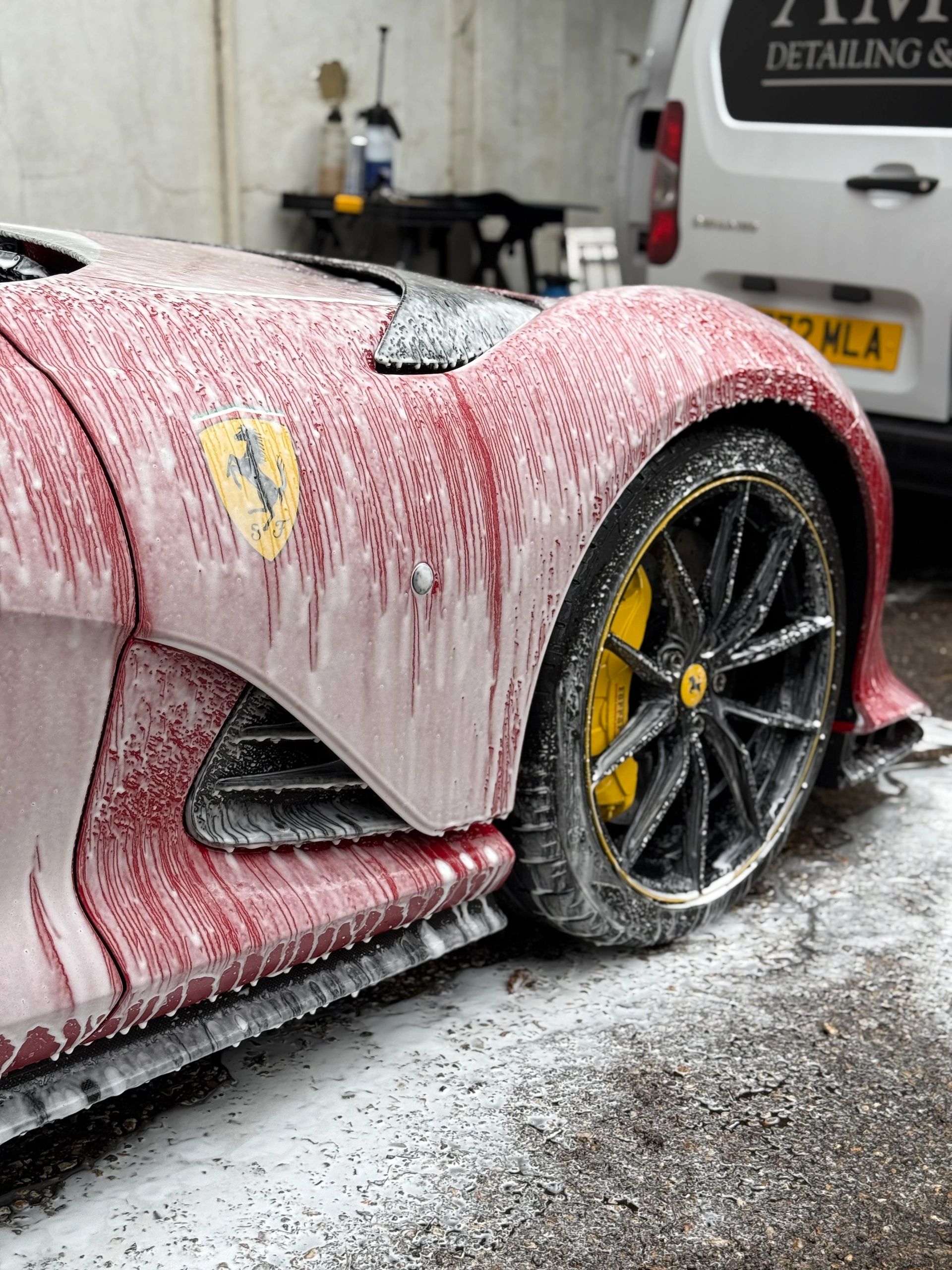 Red Ferrari covered in soap suds during a wash.