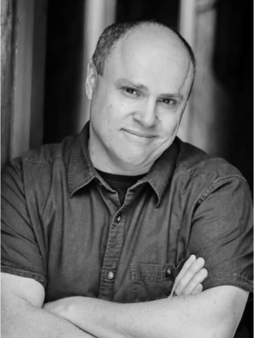 Smiling man with folded arms in black and white photo.