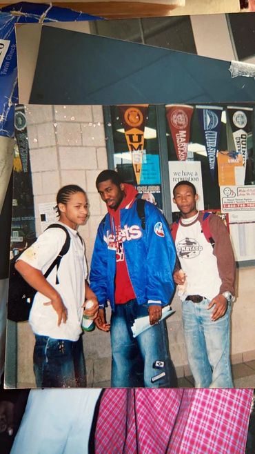Three young men posing casually in front of a wall with university pennants.