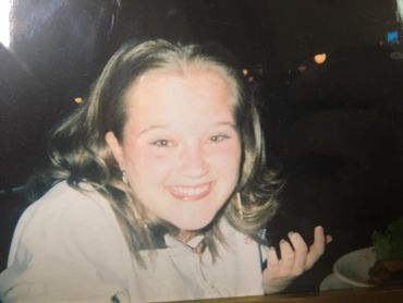 A smiling young woman with shoulder-length hair sitting at a table.