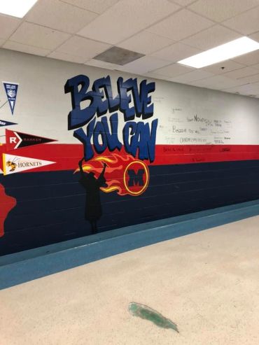 School hallway mural with motivational message and graduation cap silhouette.