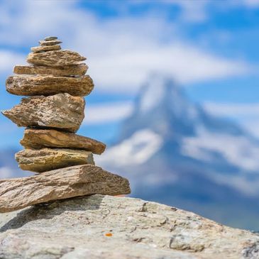 Stacked stones balanced on a rock with a mountain in the background.