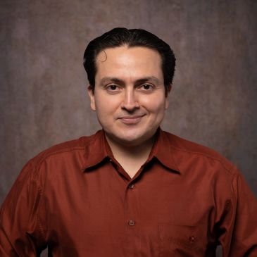 Man in a rust-colored shirt smiling at the camera.