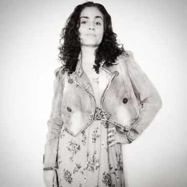 Young woman posing confidently in floral dress and denim jacket.